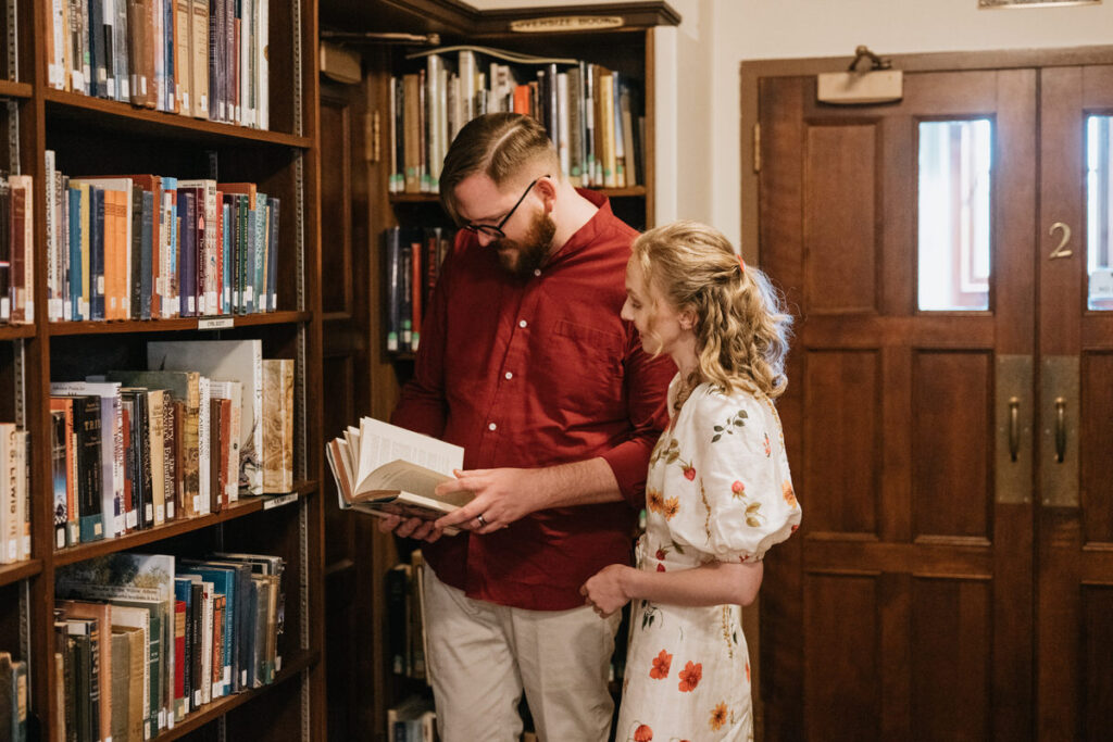 A couple standing by a bookcase looking at a book together 