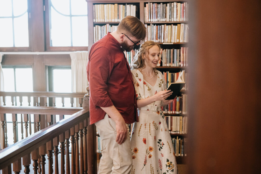 A couple standing in a library smiling and looking at a book 