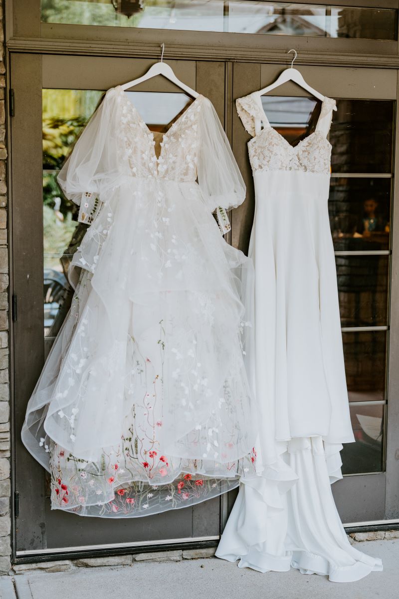 Two white wedding dresses with hangers that are hanging against a patio sliding door