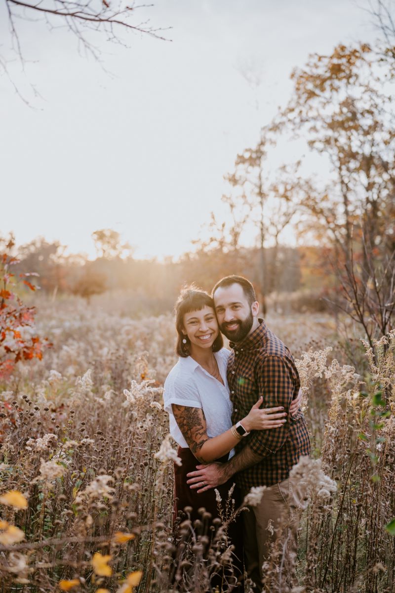 A couple standing in a field hugging each other and smiling 