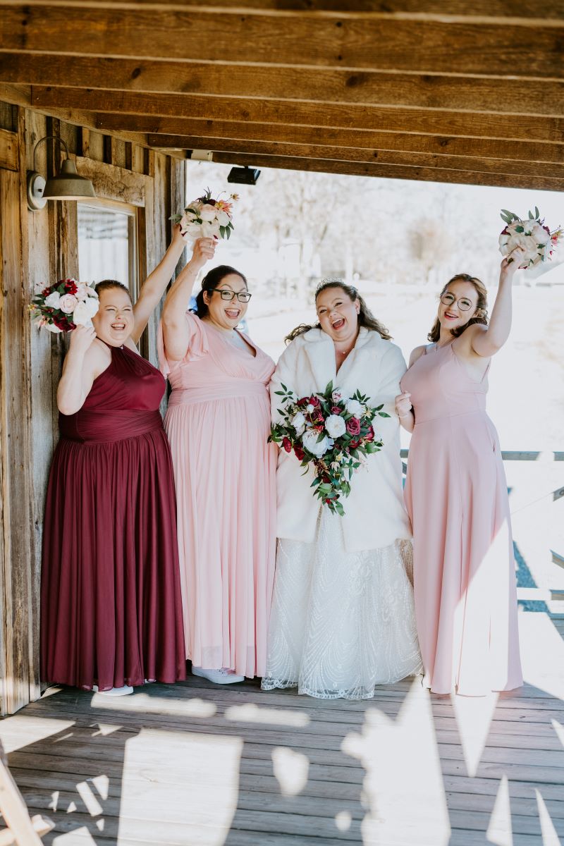 A wedding party of women standing on a deck together with their bouquets and smiling 