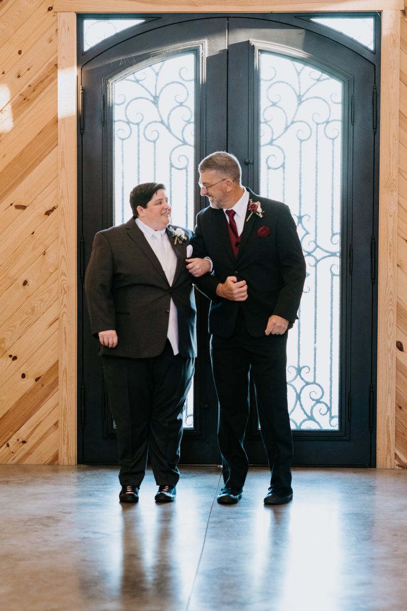 Two people making an entrance into a wedding with their arms intertwined and looking at each other