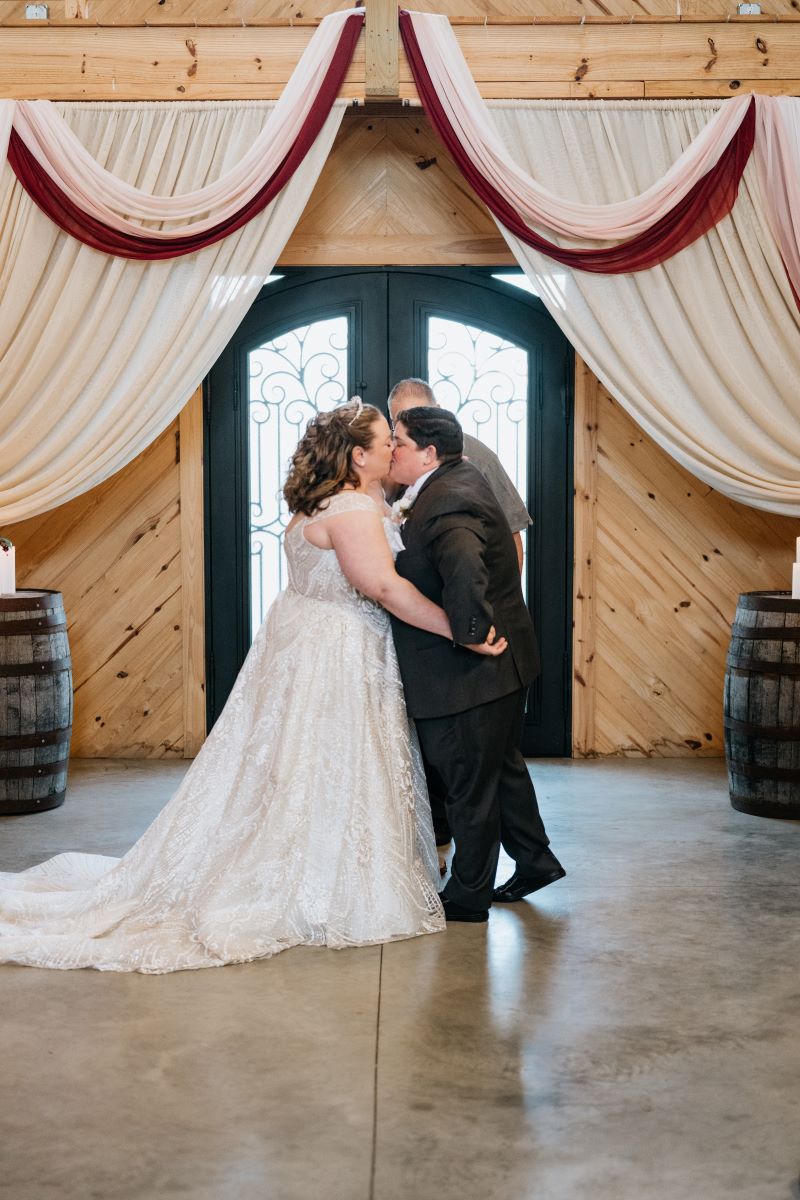 A couple kissing at their wedding ceremony with their officiant watching in the background 