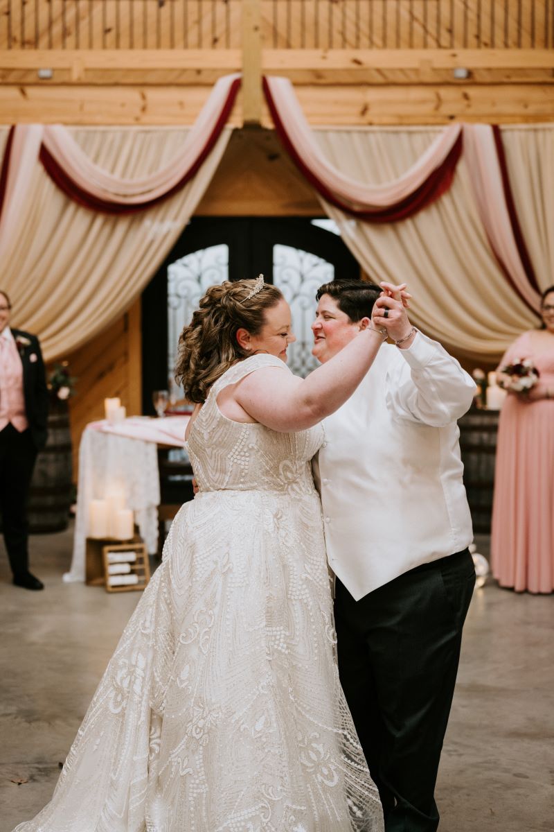 A couple dancing together at their wedding reception as their guests watch they are both smiling at each other and holding hands 