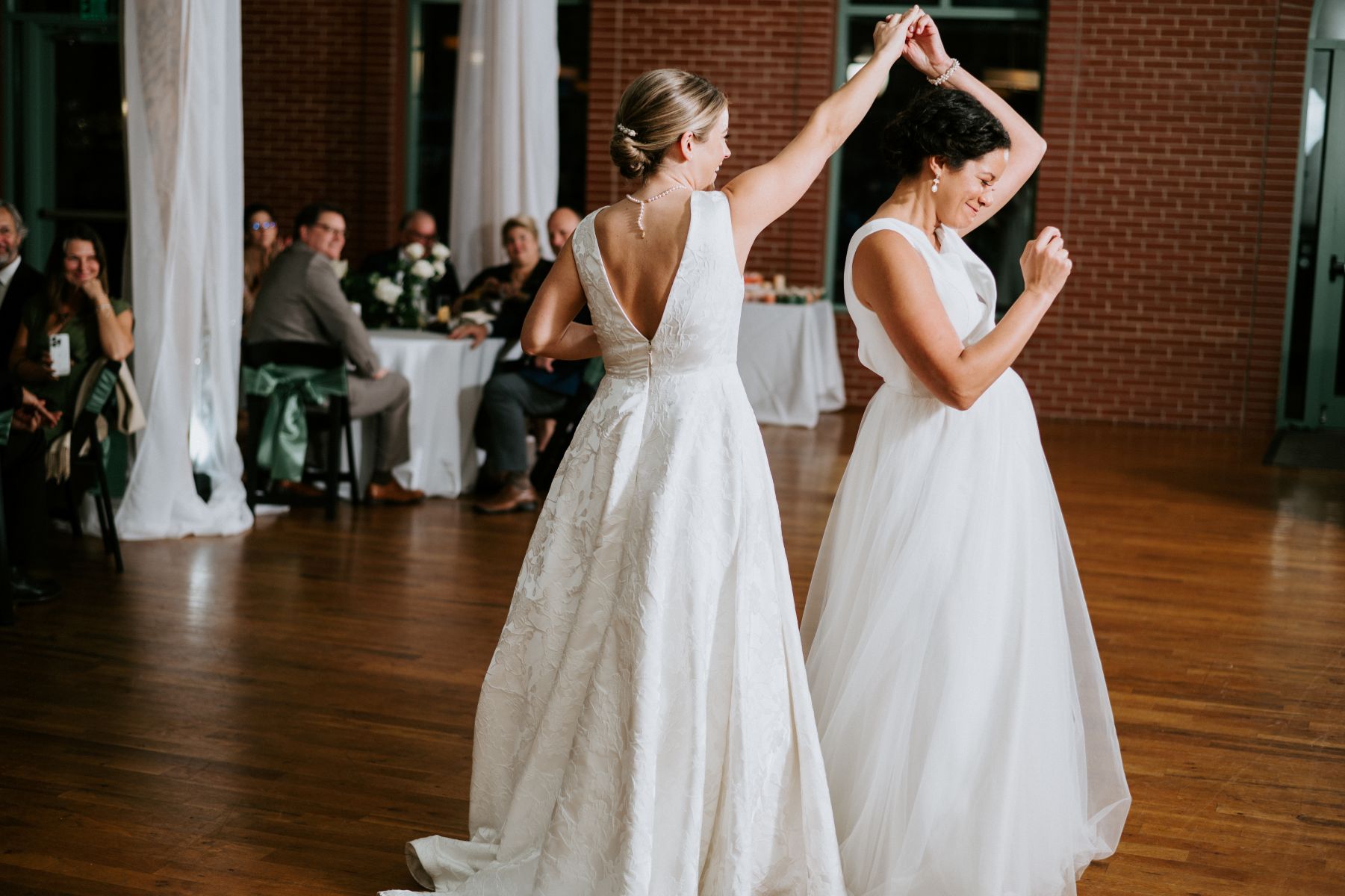 Two women in white wedding dresses at their reception sharing their first dance one woman is spinning the toher woman 