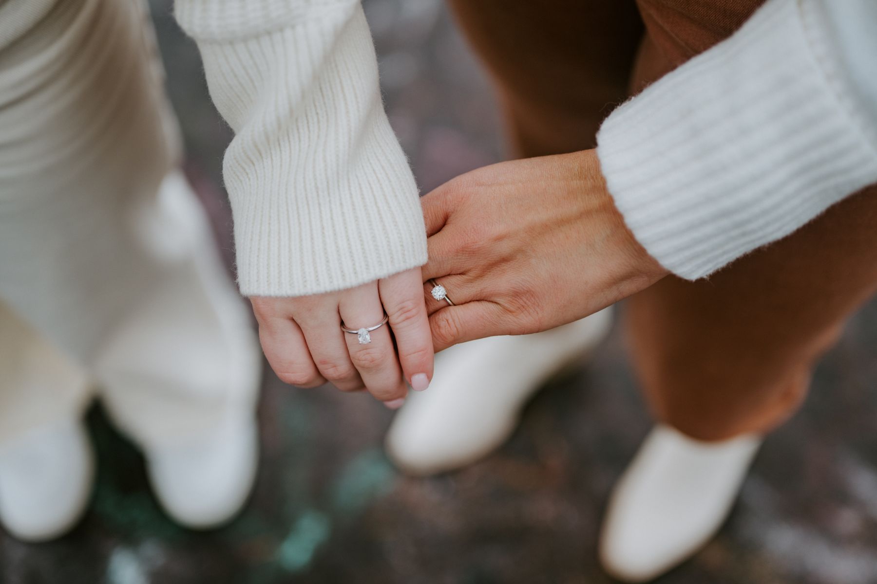 Two woemn holding hands and showing off two diamond engagement rings 