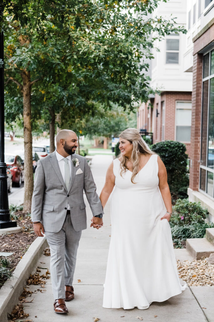 A newlywed couple holding hands and walking on a sidewalk 