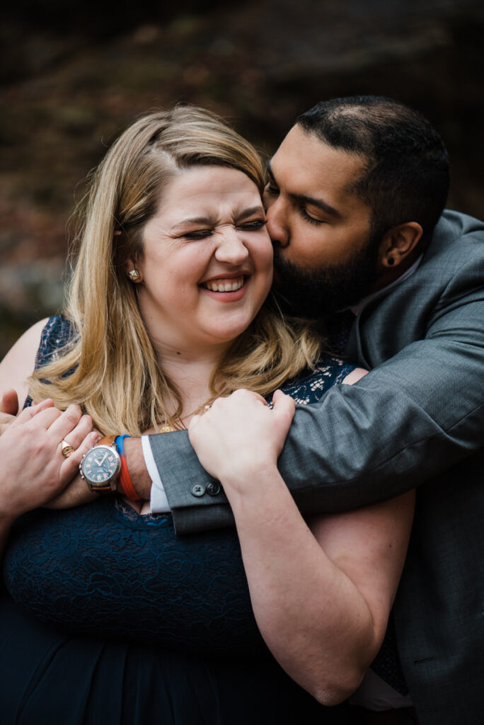 A person reaching around their partner from behind and kissing their cheek 
