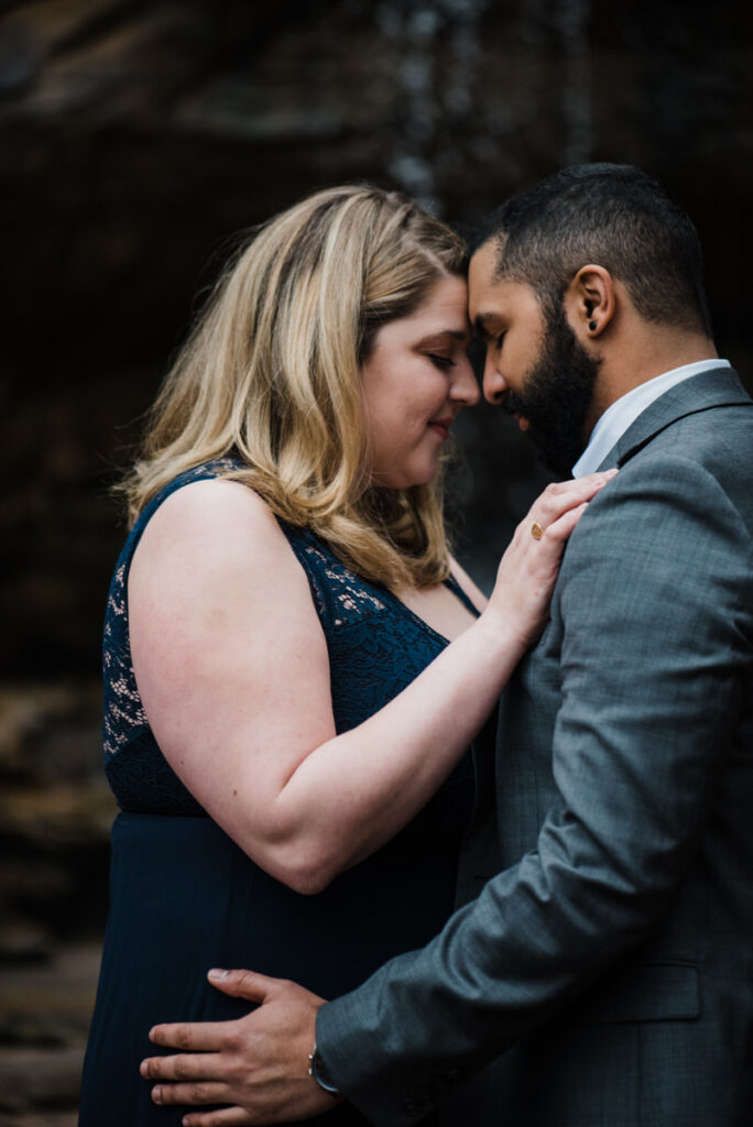 A couple standing forehead to forehead with their arms on each other 
