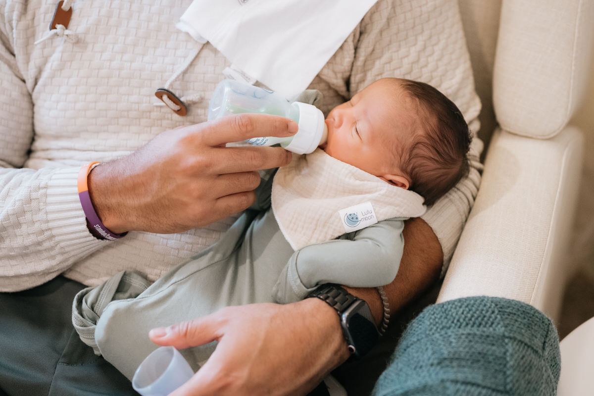 A parent sitting on a rocking chair feeding a newborn