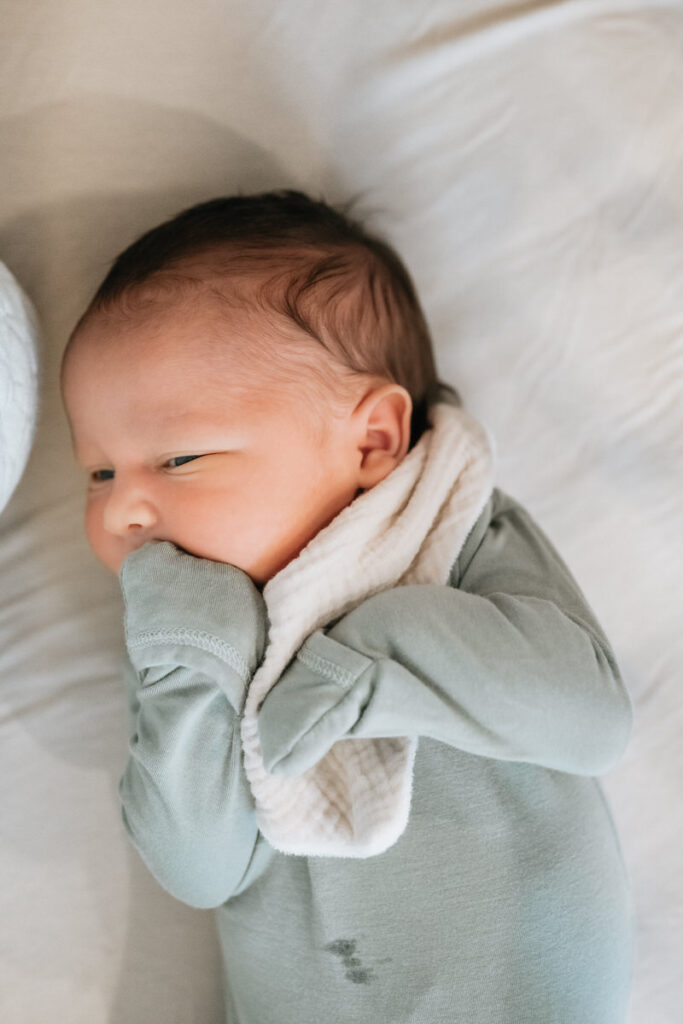 A newborn with their hands scrunched up to their face 
