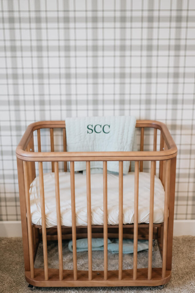 A wooden crib with a blanket over one side that has "SCC" stitched into it 