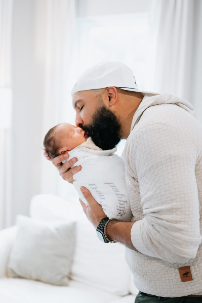 A parent holding their newborn and kissing their cheek 