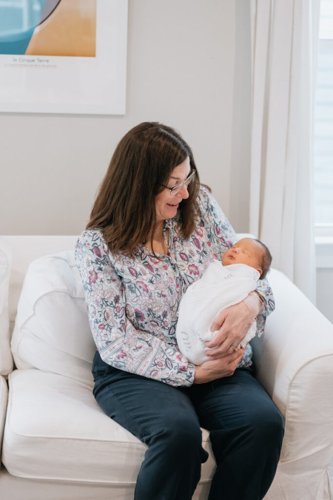 A person sitting on a white couch holding a newborn. 