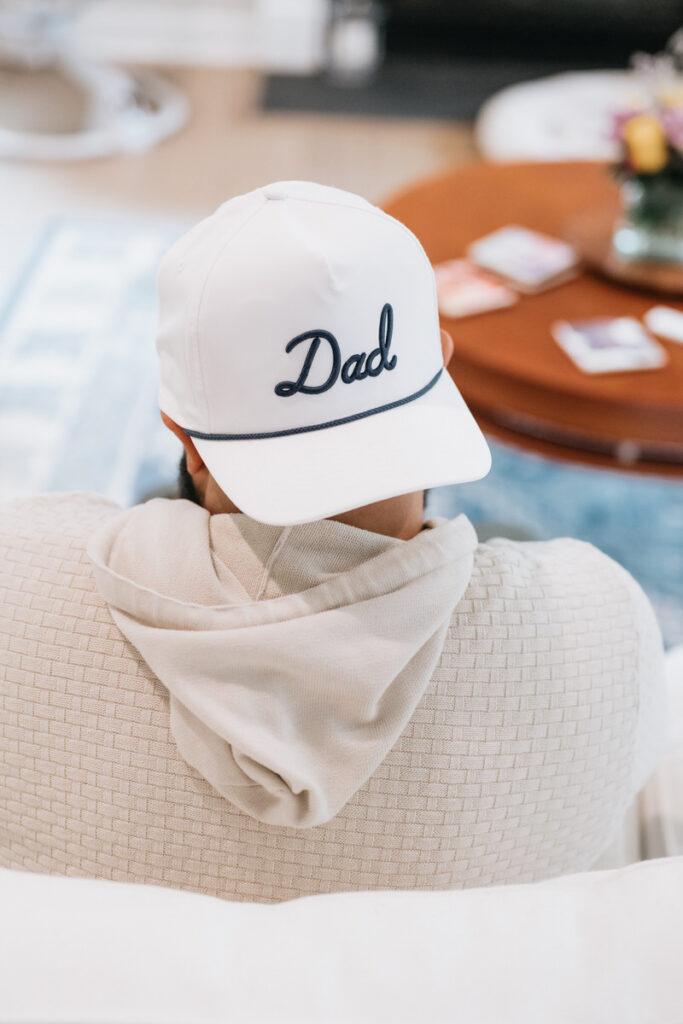 The back of a person sitting on a couch with a hat on that says "dad" 