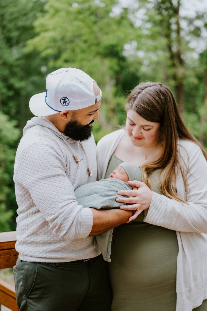 A couple standing on a deck holding a newborn in between them 