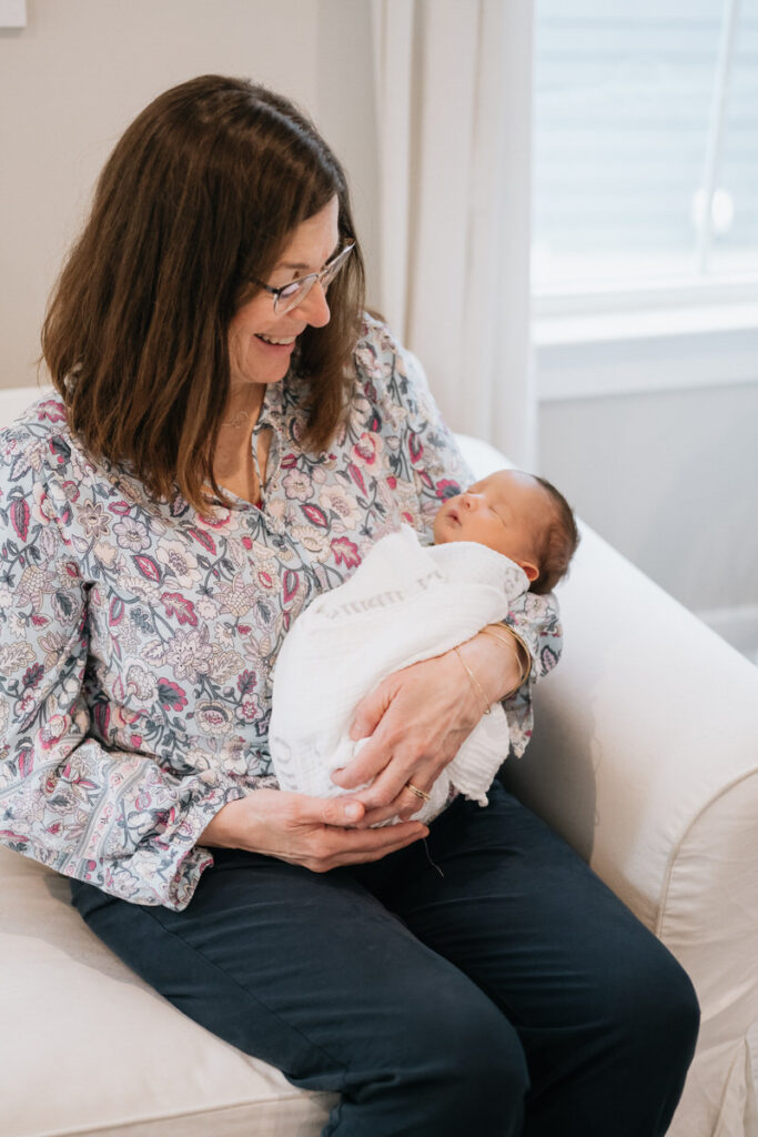 A grandparent holding their newborn grandchild while sitting on a couch 
