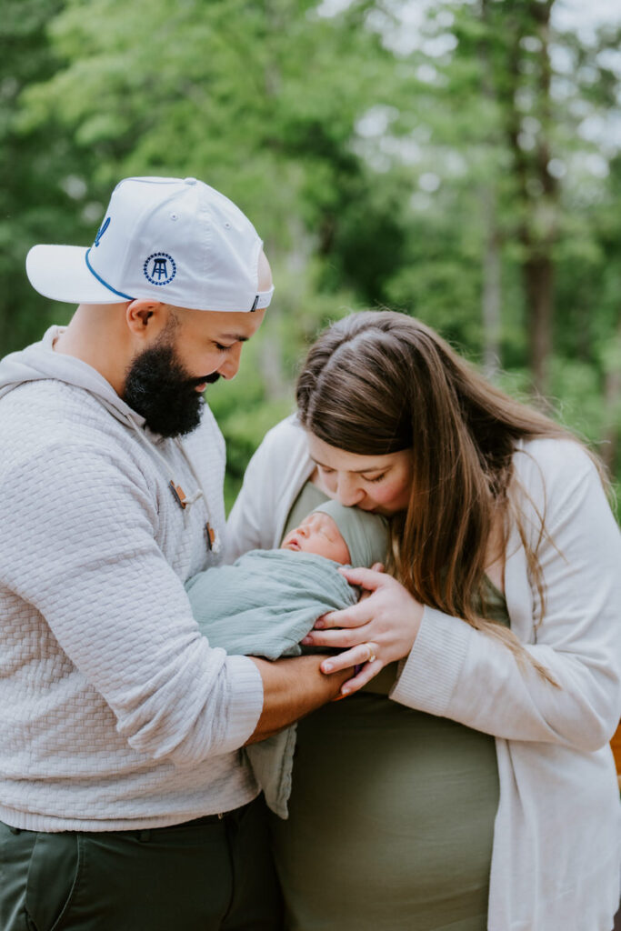 A parent kissing their newborn's head as their partner holds the baby 
