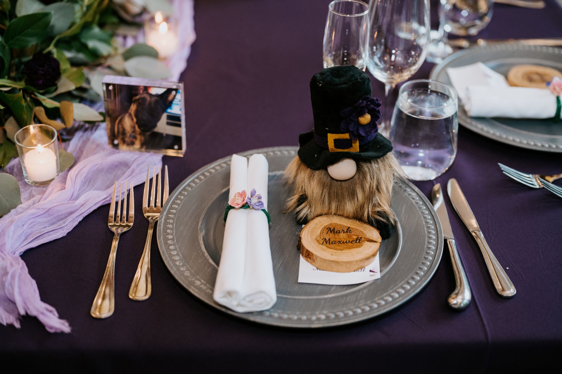wedding details at a reception on a table with a purple tablecloth, silverware, napkins, candles, and decorative items