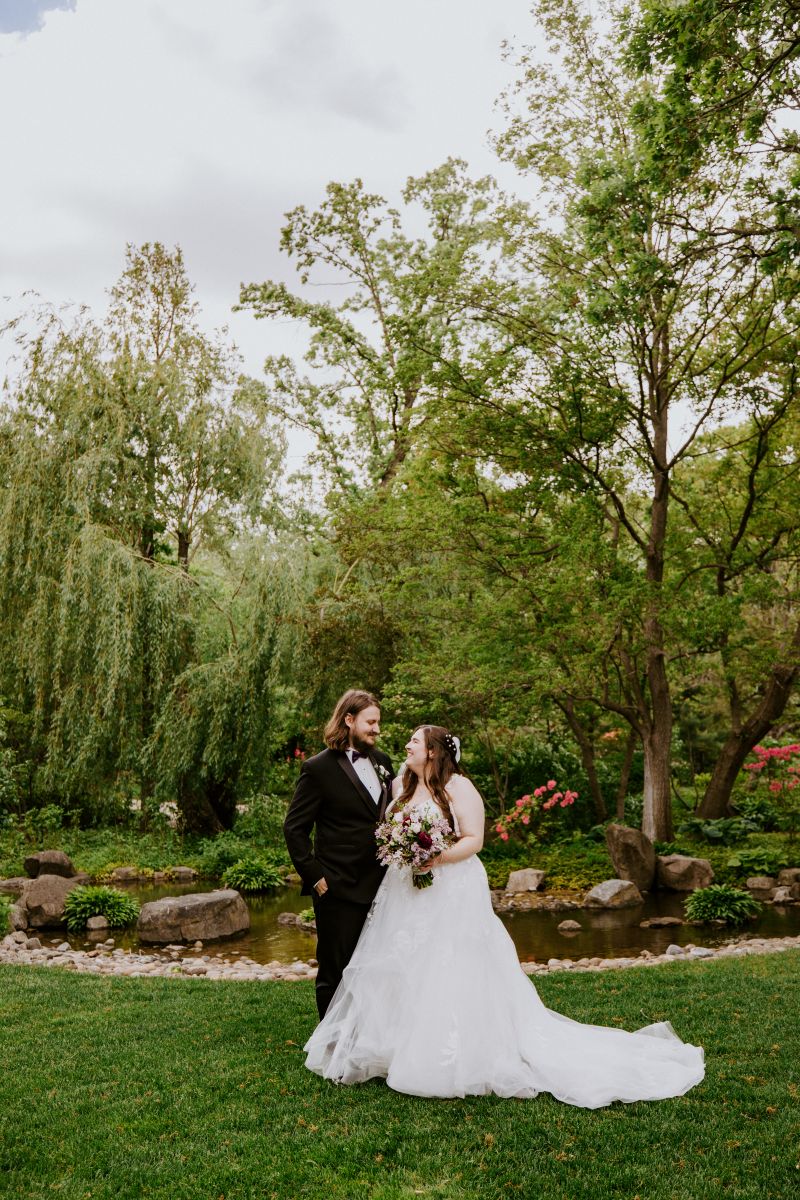 a copule looking at each other during their wedding at the Anderson Japanese Gardens the woman is wearing a white wedding dress and holding flowers the man is wearing a black suit